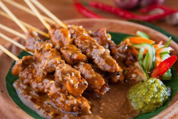 Sate Madura dengan bumbu kacang kental di sajikan di atas piring.
