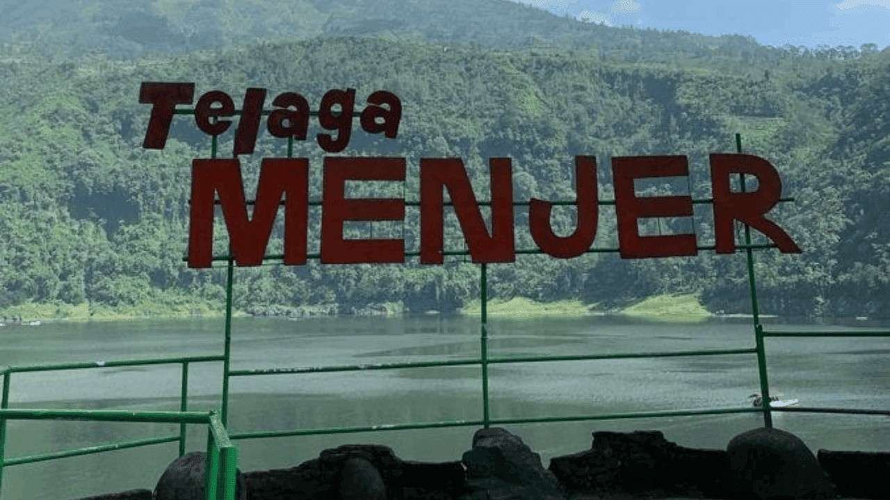 Papan nama ikonik bertuliskan "Telaga MENJER" dengan latar belakang perbukitan hijau yang asri dan permukaan air telaga yang tenang.