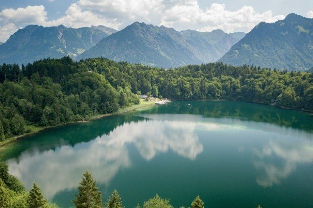Pemandangan Telaga Menjer dengan air yang tenang dikelilingi perbukitan hijau dan pegunungan, menciptakan suasana alam yang sejuk dan menenangkan.